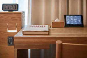 A modern minimalist desk with a wooden top and a clock, tissue box, and tablet with smart home controls.