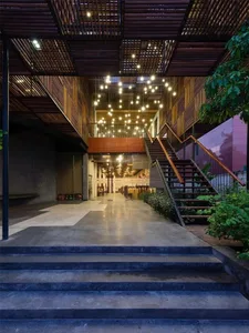 Atrium with concrete steps, stone walls, and steel handrails, illuminated by warm pendant lights and natural light.