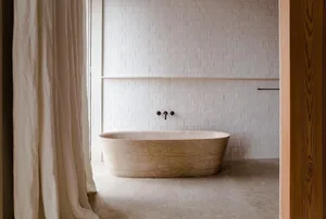 Modern minimalist bathroom with a sandstone bathtub, white tiled walls, and a wooden door.