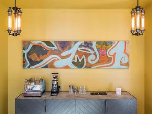 A modern coffee bar featuring a metal counter with a stainless steel espresso machine and a large colorful painting on the wa