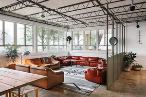 A spacious industrial living room with large leather sofas, concrete flooring, and exposed steel beams on the ceiling.