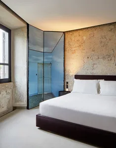 Modern minimalist bedroom with concrete walls and floor, featuring a white bed and simple decor.