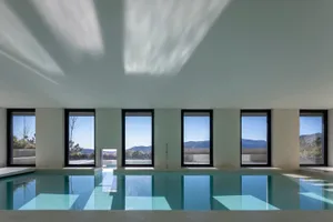 Modern industrial-style indoor swimming pool with concrete walls and floor, featuring large windows overlooking scenic mounta