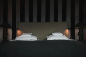 Modern minimalist bedroom with a double bed, white pillows, and a striped grey and black wall.