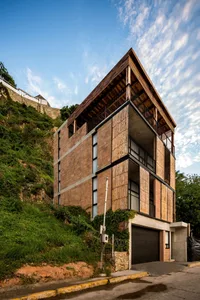 Modern residential building with a combination of wooden panels, bricks, and concrete, situated on a hillside.