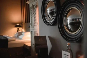 A cozy hotel suite bedroom with a warm ambiance, featuring a single bed, nightstand, and decorative mirror wall.