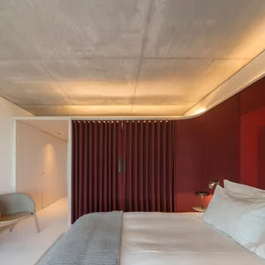 Bedroom interior with concrete ceiling, red curtains, and minimalist design elements.