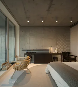 Modern minimalist bedroom with concrete walls, a large bed, and a sleek desk.