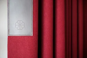 A close-up of a modern red curtain with a metallic plate featuring a flower emblem.