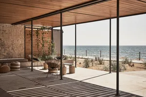 Modern beach terrace with wooden roof structure and concrete flooring, overlooking the ocean.