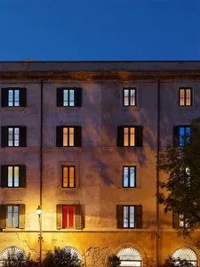 A stone building facade illuminated at dusk with lights on inside several windows.