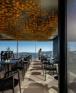 A modern restaurant interior featuring a concrete ceiling adorned with small, golden leaf-shaped elements.