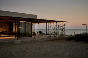 A modern residential beach house featuring a metal and glass exterior at dusk.