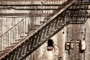 Rusted metal staircase on an abandoned industrial exterior with concrete walls.