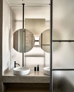 Minimalist bathroom with concrete finishes, modern sink, and circular mirrors