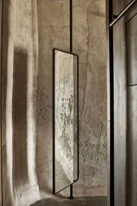 A minimalist interior design featuring metal-framed floor-to-ceiling mirror with a concrete wall backdrop.