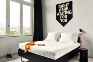 A minimalist bedroom featuring a white bed with a black headboard and a black table lamp, with a banner reading 'Right Here W