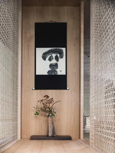 A minimalist interior design featuring a wooden frame, a black scroll with abstract calligraphy, and a floral arrangement.