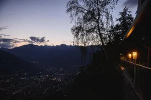 A nighttime landscape featuring a silhouette of mountains and illuminated city lights.