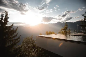 Two people enjoying an infinity pool with a stunning view of mountains during sunset.