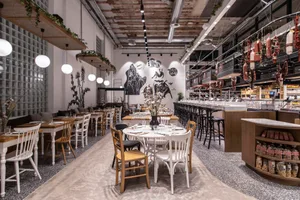 A modern cafe dining room with wooden tables, concrete flooring, and glass walls and shelves.
