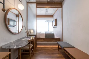 A minimalist bedroom featuring a concrete floor, wooden furniture, and a marble table with a vase of flowers.
