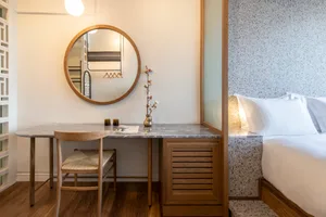 Minimalist bedroom with marble table and bed, wooden chair, and a round mirror.