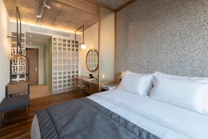 A minimalist bedroom with white walls, a large bed, and a desk area with a panel wall.