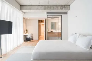 A minimalist bedroom with a white bed, white curtains, and a white desk in the background.
