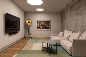A modern living room featuring a beige sectional sofa, coffee tables, a flat-screen TV, and minimalist decor.