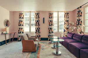 A modern living room with a purple sofa, patterned curtains, and a glass coffee table.