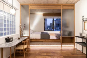 An elegant, minimalist bedroom featuring wood and glass materials, with a bed, desk, and a view of the city through frosted g