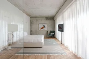 A modern minimalist bedroom with a concrete wall, white bed, and white curtains.