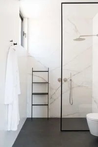A minimalist bathroom featuring white marble walls and a black ladder shelf.