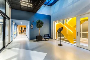 Modern office hallway with glass walls, concrete floor, and yellow staircase.