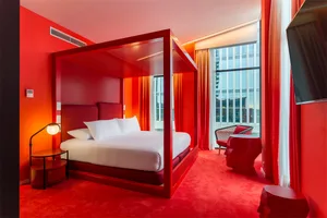 A modern hotel room with a red theme, featuring a metal frame canopy bed and red carpeting.