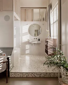 A minimalist bathroom with a terrazzo floor, a floating wooden vanity, and a round mirror.