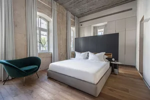 Modern minimalist bedroom with concrete walls, wood flooring, and a large window.