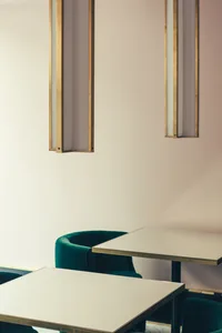 Minimalist restaurant interior with metallic accent lighting, green velvet upholstery, white walls and ceiling, and vinyl tab