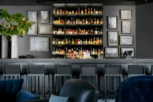 Modern bar interior with sleek metallic shelving, glass bottles, leather seating, stone countertops, and wooden accents.