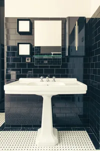 A modern bathroom featuring a black-tiled wall and a white pedestal sink.
