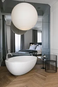 Modern bathroom with ceramic bathtub and metal accents, featuring a spherical light fixture and large mirrors.
