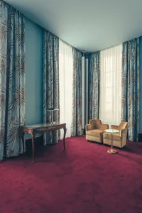 A modern living room with blue curtains, brown chairs, and a red carpet.