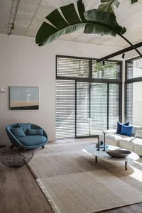 A modern living room with a white concrete wall, wooden flooring, and a low-profile sofa and armchair.