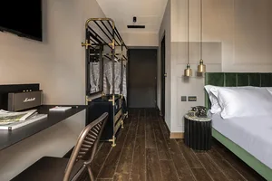 A modern bedroom featuring a green upholstered bed, wooden flooring, and brass accents.