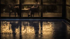 A serene image of raindrops falling on a glass window, with a reflection of the room interior.