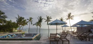 Poolside lounge area with umbrellas, deck chairs, and palm trees overlooking the ocean.