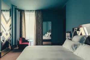 A contemporary hotel room with textured and patterned wallpaper, a bed with white bedding, and a red armchair.