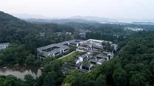 Aerial view of traditional residential buildings surrounded by lush greenery and a serene lake.