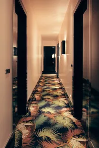 A vibrant, tropical-themed carpet adorns a hotel corridor with decorative lighting fixtures.